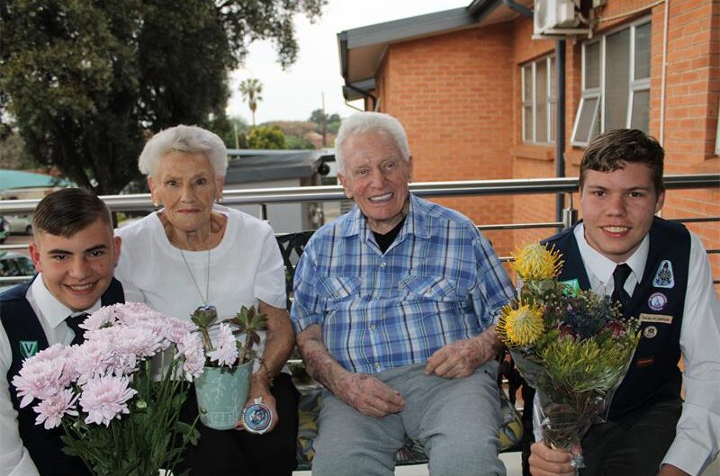 Twee jong seuns hou blomme aan bejaarde man en vrou
