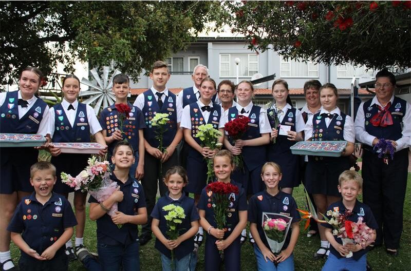 Groep kniders in univorms wat blomme en kolwyntjies vas hou