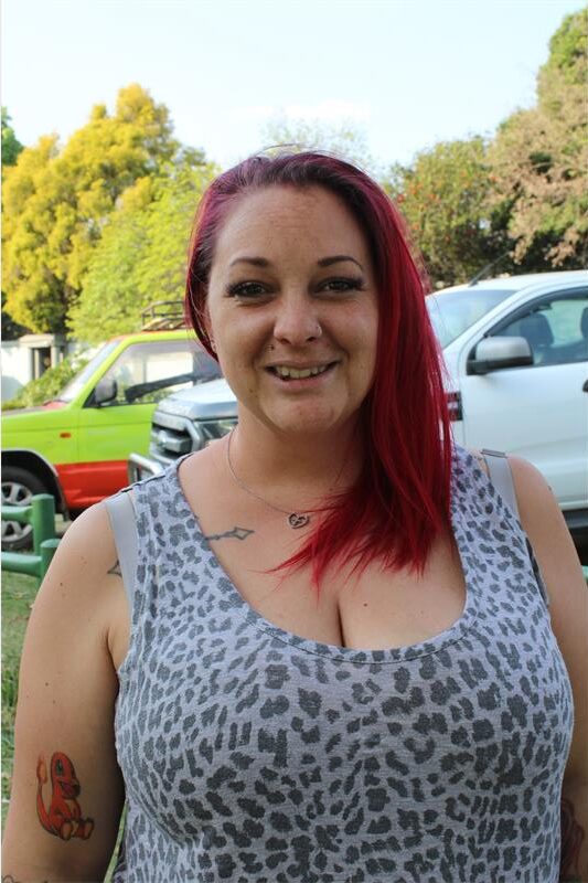White woman with red hair standing in front of cars