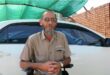 Bearded white man sitting in a wheelchair in front of a white car