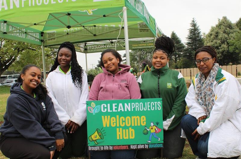 Group of four black girls with a black woman, posing at a community clean-up board