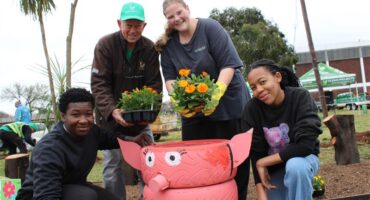 Elderly man stands with three youths at a pig made from tyres holding orange and yellow seedlings