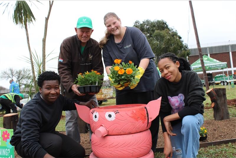 Elderly man stands with three youths at a pig made from tyres holding orange and yellow seedlings