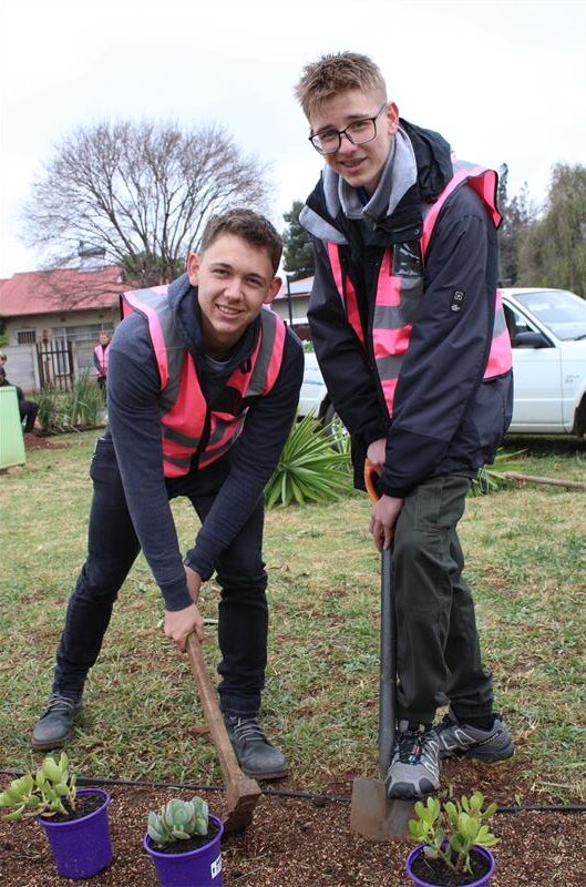 Two boys wearing pink reflective jackets digging into a flower bed