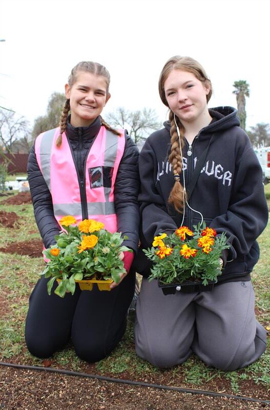 Two girls pose holding yellow and orange seedlings