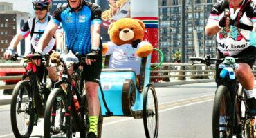 Cyclist with a teddy bear on the back of a bike, taking part in a race.