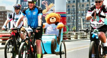 Cyclist with a teddy bear on the back of a bike, taking part in a race.