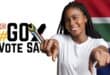 A young black female with dreadlocks pointing into the camera wearing a white T-shirt with a cross and the words go vote SA and the SA flag colours next to her.