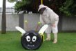 Man wearing a bee suit standing next to a bee made out of tyres