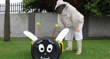 Man wearing a bee suit standing next to a bee made out of tyres