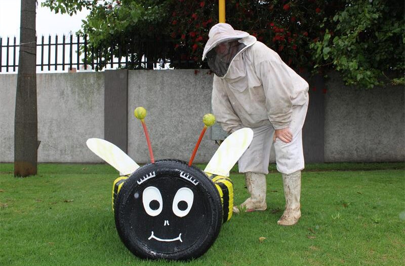 Man wearing a bee suit standing next to a bee made out of tyres