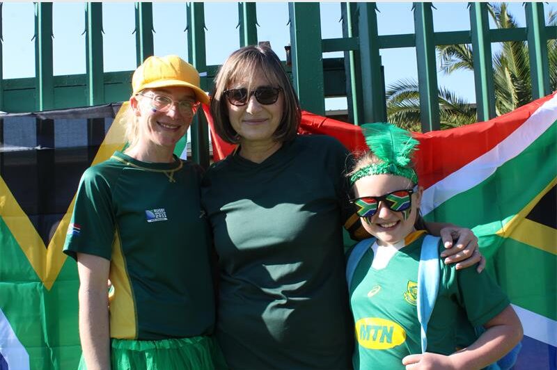 Two women and a girl standing in front of a South African flag