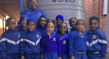 Educator stands with a group of uniformed children at a water tank
