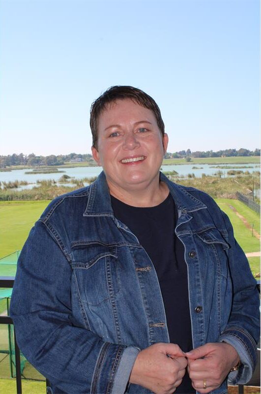 Short-haired woman wearing denim jacket standing on a balcony over looking a dam