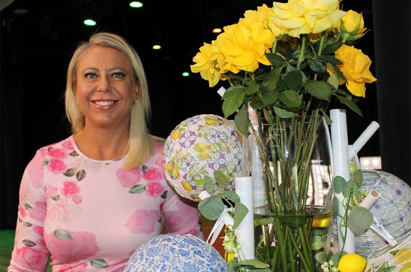 Blonde woman wearing pink standing next to yellow roses