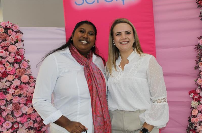Two women standing in front of a pink backdrop