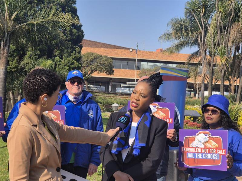 A black woman being interviewed by a white woman with other people in the background.