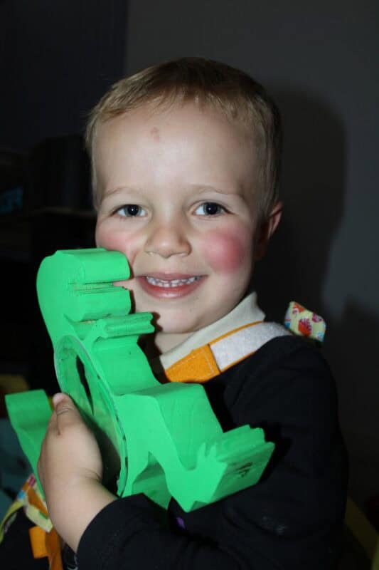 Little boy holding a green wooden cdinosaur