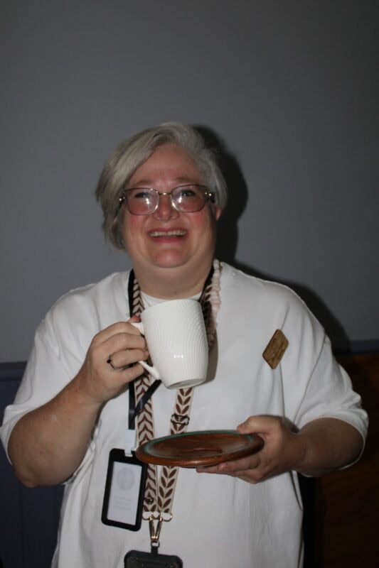 Woman with grey hair holding a mug and wooden saucer