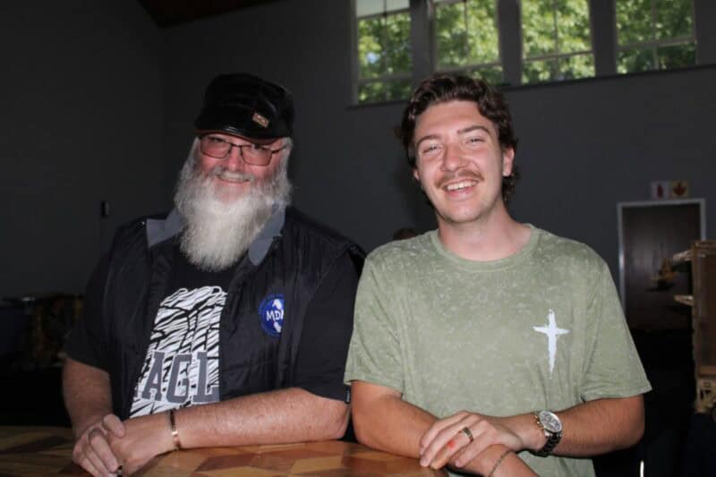 Two men leaning on a wooden table