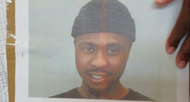 Picture of a black man wearing a beaning with a black hand resting on the edge of the photo