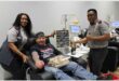 A man in a blood donation chair flanked by SANBS staff.
