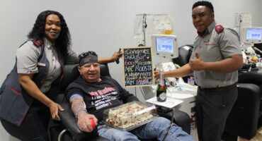 A man in a blood donation chair flanked by SANBS staff.