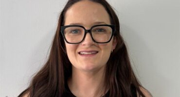 Woman with long dark hair wearing glasses smiling