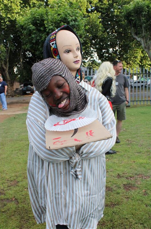 Black boy with his head on a plate, closes his eyes and sticks his tongue out with a plastic head in the background