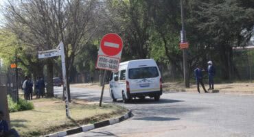 Road sign indicating a temporary one-way, with times displayed and a white mini bus driving past it