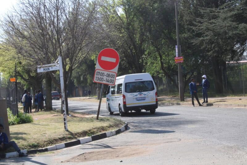 Road sign indicating a temporary one-way, with times displayed and a white mini bus driving past it
