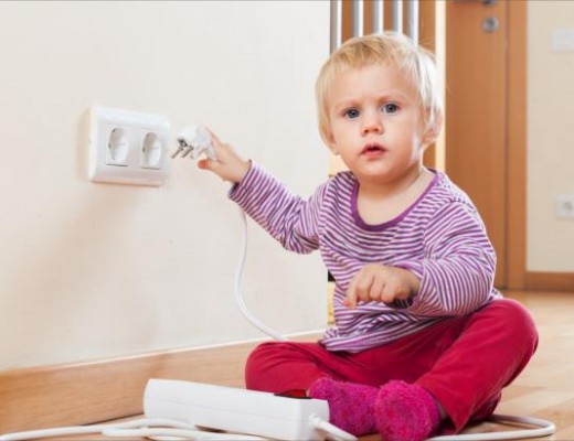 Baby playing with electrical extension and outlet on floor