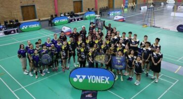 A group of people posing for a photo on a badminton court.