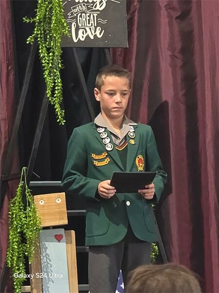 A boy in a green jacket is standing on a stage.