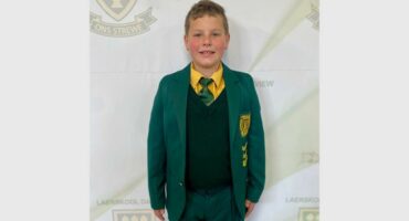 A boy in a school uniform standing in front of a wall.