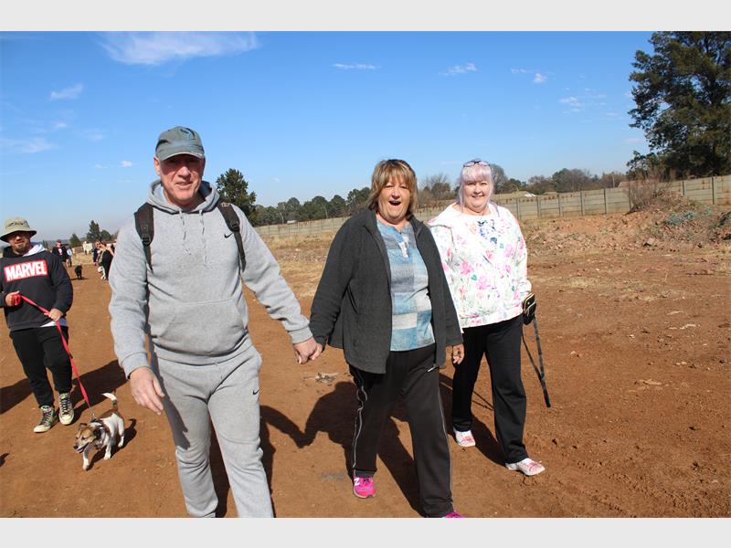 Three people walking on a dirt road with a dog.