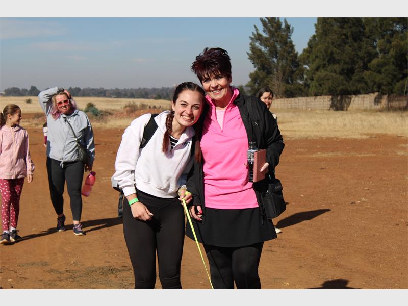 Two women in pink shirts and black pants standing next to each other.