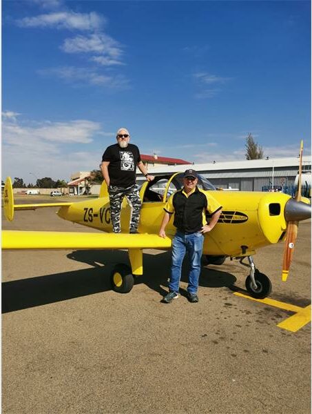 Two men standing next to a small yellow airplane.