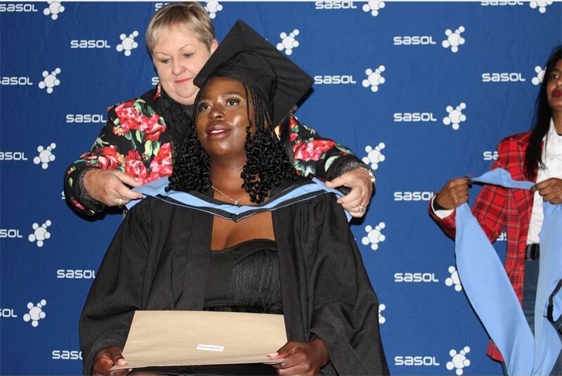 A woman in a graduation gown is getting her diploma tied.