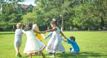 Children playing and holding hands in a park during sunny weather for community family activities.