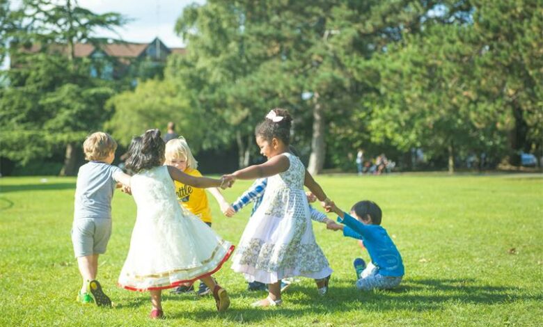 Children playing and holding hands in a park during sunny weather for community family activities.