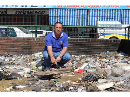 Ward 75 councillor, Clr Dean Stone, crouches on a pile of rubbish dumped on the lawn of the War Memorial's garden.