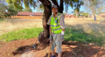 A man in a safety vest and work boots standing next to a tree.