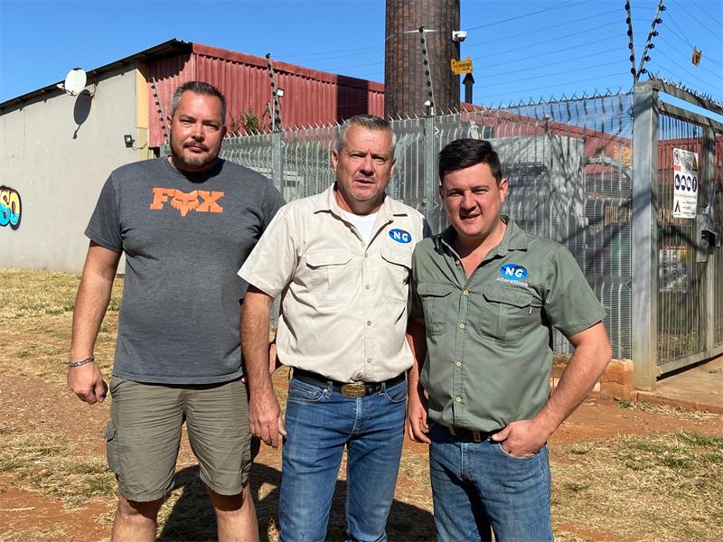 Three men standing in front of a fence.
