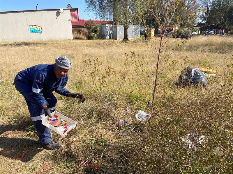 A man in blue overalls picking up trash in a field.