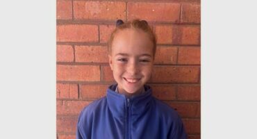A young girl in a blue jacket standing against a brick wall.