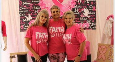 Three women wearing pink shirts standing next to a banner.