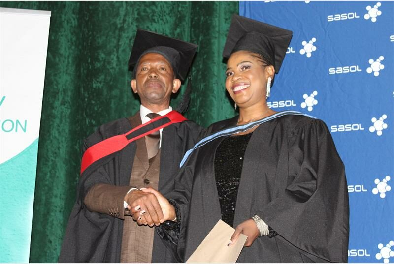 A man and woman in graduation gowns shaking hands.