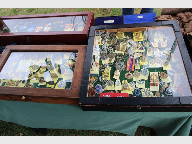 Display of military badges in two wooden cases with glass tops at an outdoor market. Each case shows various insignia on a green cloth background.