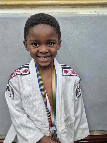 Smiling young boy in judo gi with medals at Springs Advertiser event.
